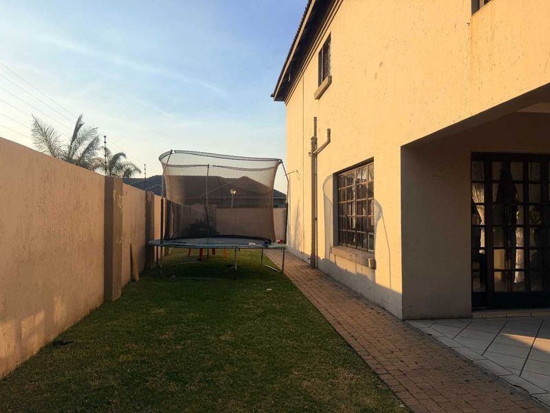 A view of the rear exterior of the house featuring a paved walkway, a small lawn area, and a covered patio entrance.