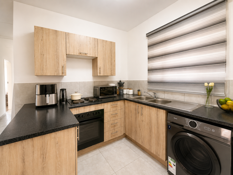 Modern kitchen featuring light wood-look cabinetry, dark laminate countertops, built-in oven with electric hob, and a double bowl stainless steel sink.