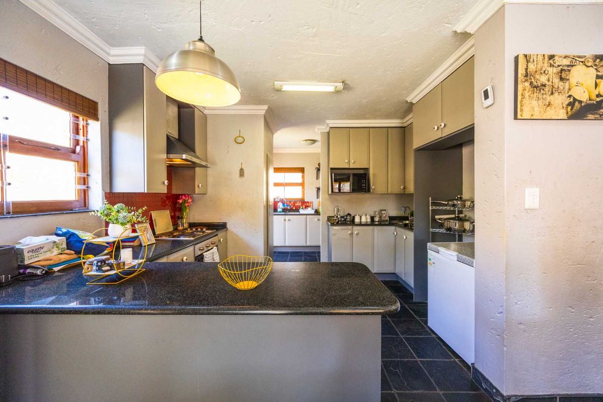 A functional kitchen featuring granite countertops, built-in cabinetry, and tiled flooring, with a convenient layout and direct access to an adjacent scullery area.