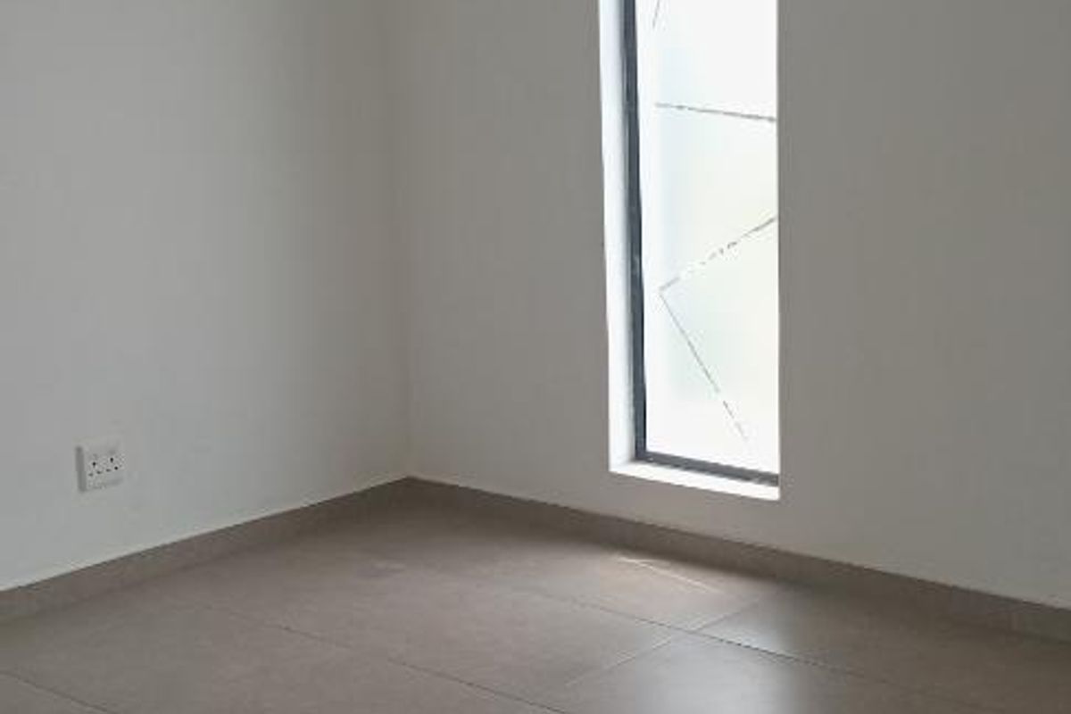 A bright, empty room featuring neutral floor tiles, clean white walls, and a tall, narrow window providing natural light.