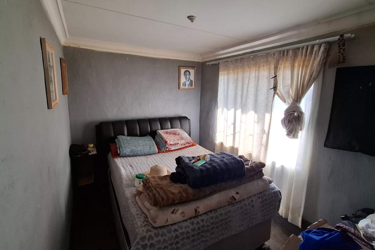 A compact bedroom featuring grey textured walls, ceiling cornicing, and a window with a curtain rail.