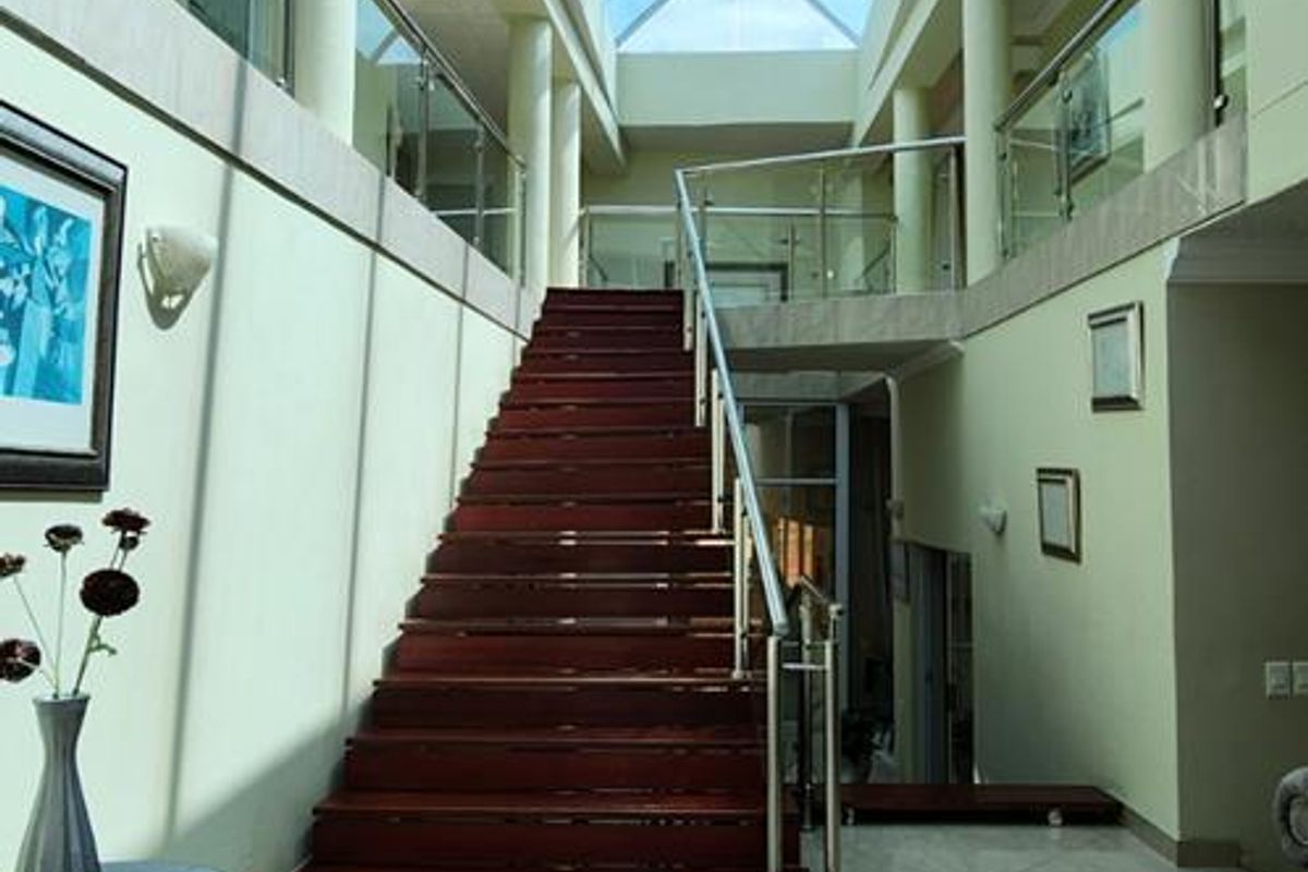 Spacious grand entrance hall featuring a large glass skylight, polished tiled flooring, and a prominent staircase with a modern glass balustrade.