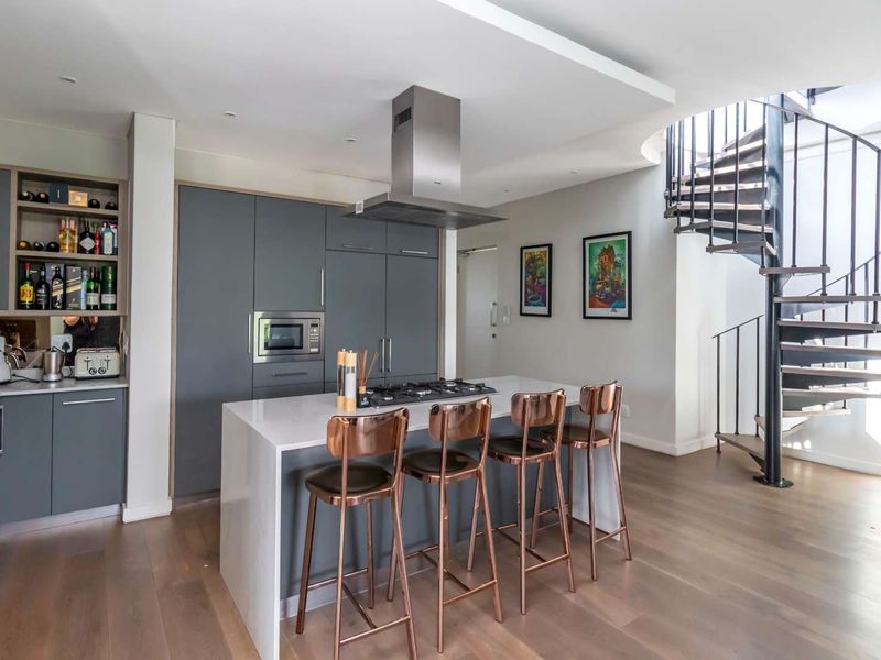 Modern kitchen featuring a central island with gas cooktop, integrated appliances, sleek cabinetry, and a striking spiral staircase leading to the upper level.