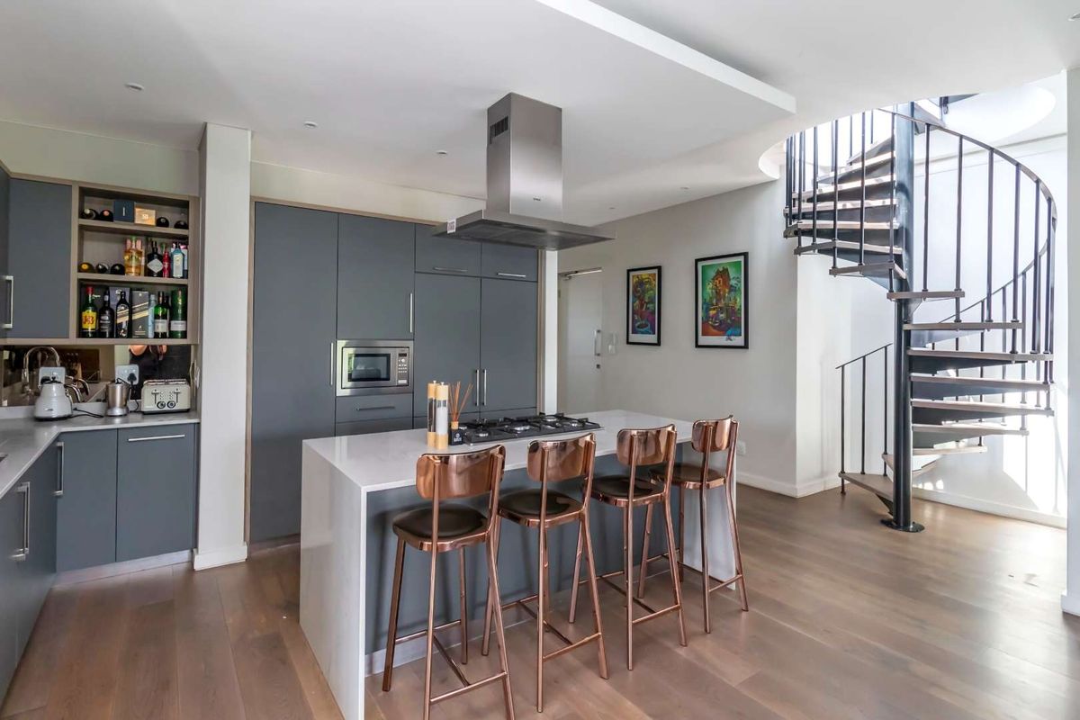 Modern kitchen featuring a central island with gas cooktop, integrated appliances, sleek cabinetry, and a striking spiral staircase leading to the upper level.