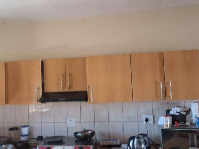 A functional kitchen area featuring laminate cabinetry, a built-in extractor fan, and a tiled backsplash, requiring some cosmetic updates to improve its overall condition.
