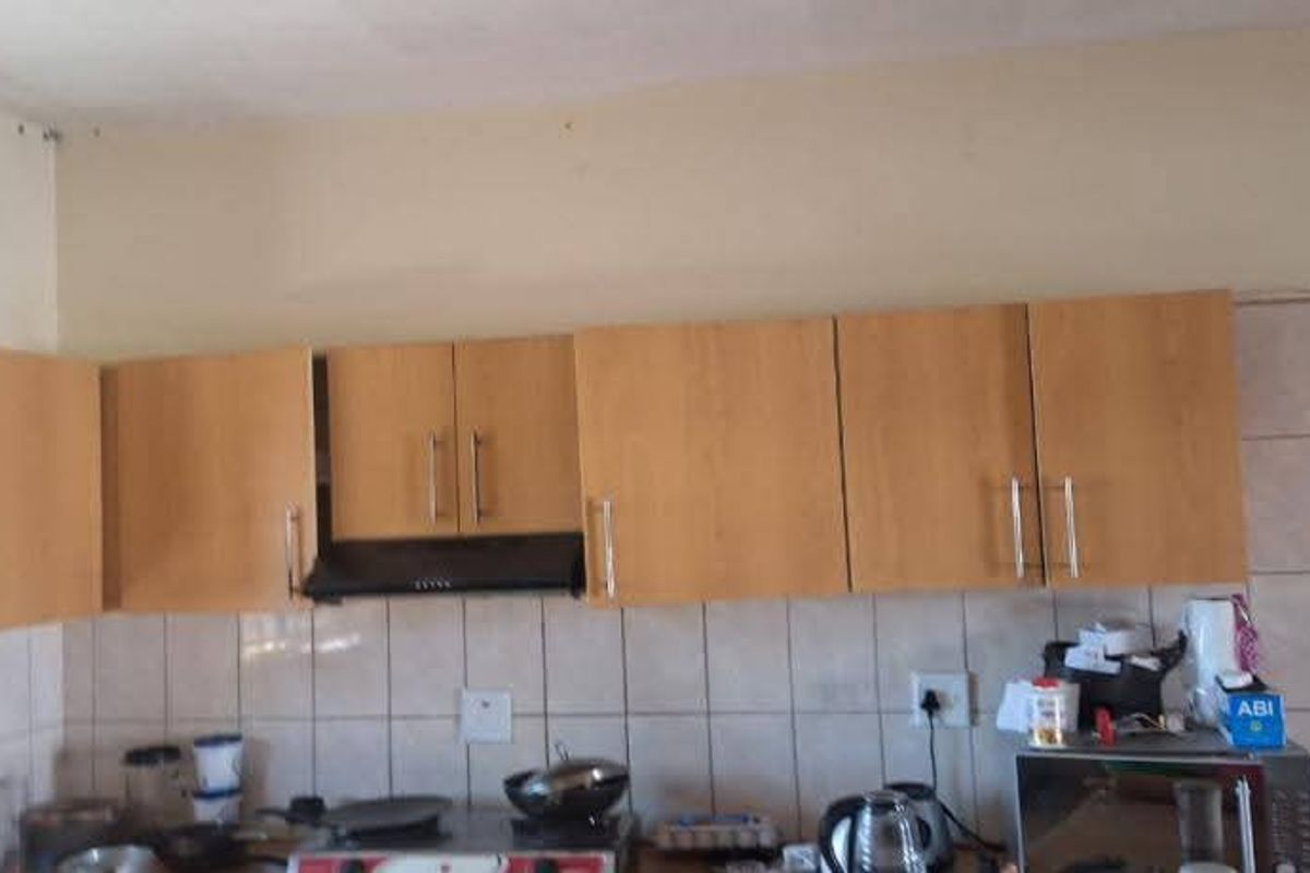 A functional kitchen area featuring laminate cabinetry, a built-in extractor fan, and a tiled backsplash, requiring some cosmetic updates to improve its overall condition.