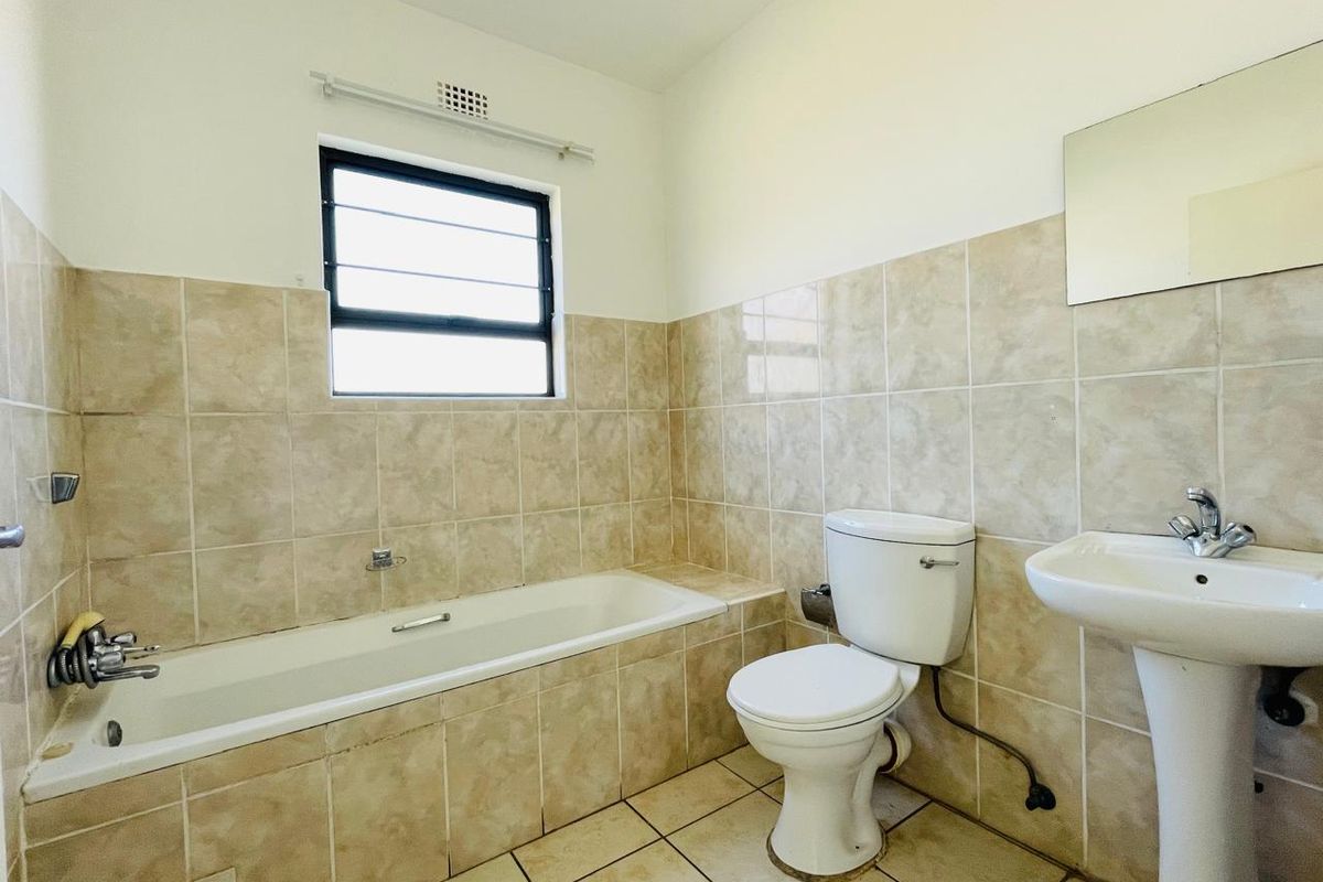 A functional bathroom featuring a built-in bathtub, pedestal sink, and toilet with neutral wall and floor tiling.