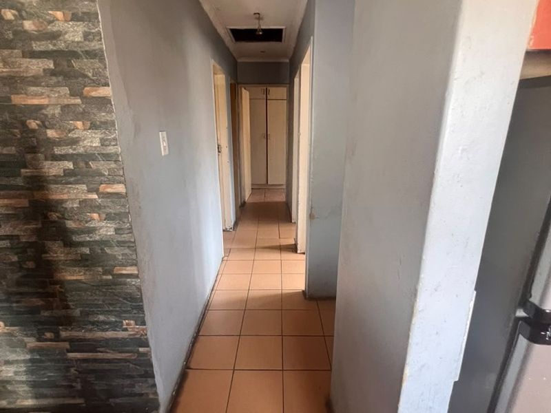 A narrow hallway featuring tiled flooring, a stone accent wall, and recessed ceiling lighting, leading towards built-in storage cupboards.
