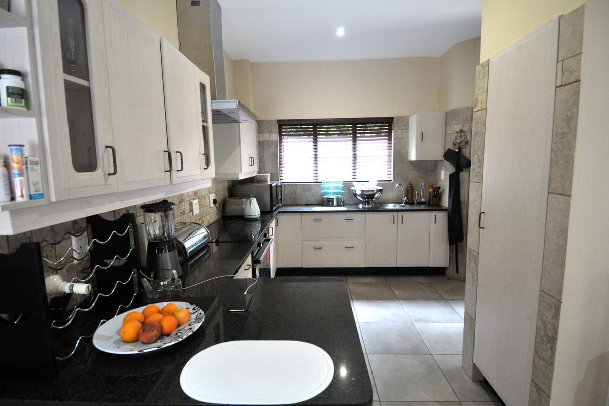 A functional kitchen featuring dark granite countertops, light-toned cabinetry, tiled backsplash, and tiled flooring, offering ample storage and workspace.