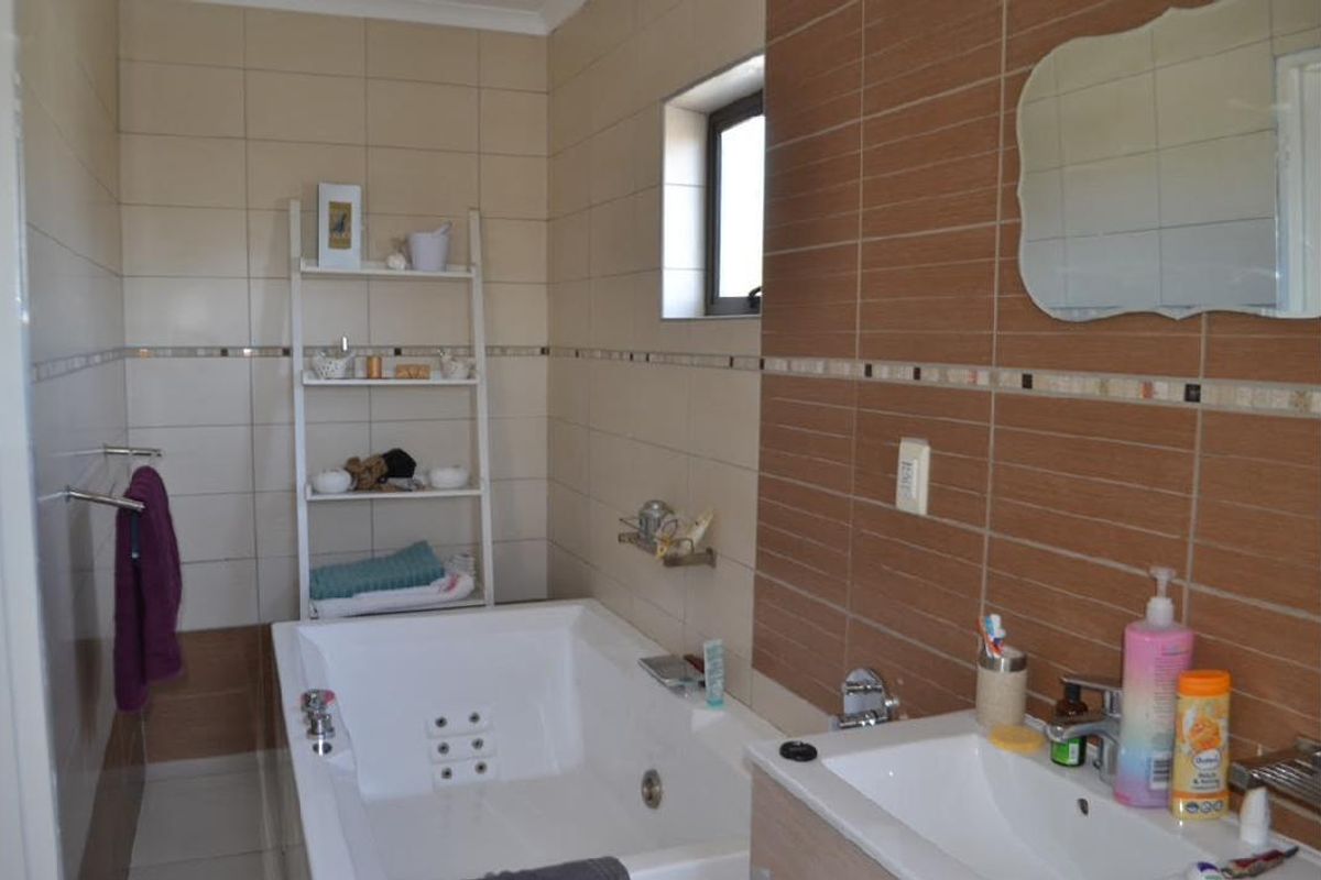 A functional bathroom featuring a built-in bathtub, wall-mounted vanity basin, and tiled wall finishes with a decorative mosaic border.