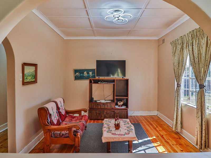 A cozy living room featuring original hardwood flooring, a distinctive arched entryway, and classic ceiling tiles, offering a warm and traditional atmosphere.