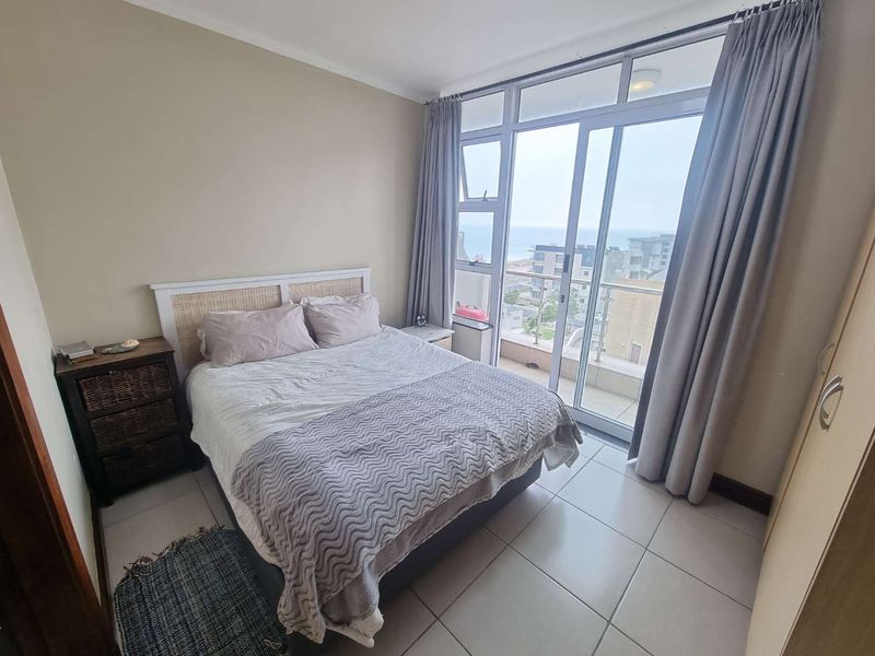 A bedroom featuring tiled flooring, built-in wardrobe, and large sliding glass doors providing access to a balcony with coastal views.