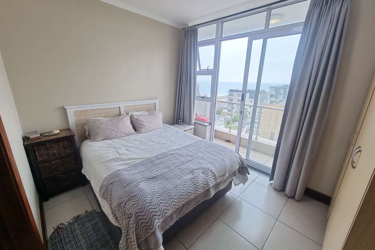 A bedroom featuring tiled flooring, built-in wardrobe, and large sliding glass doors providing access to a balcony with coastal views.