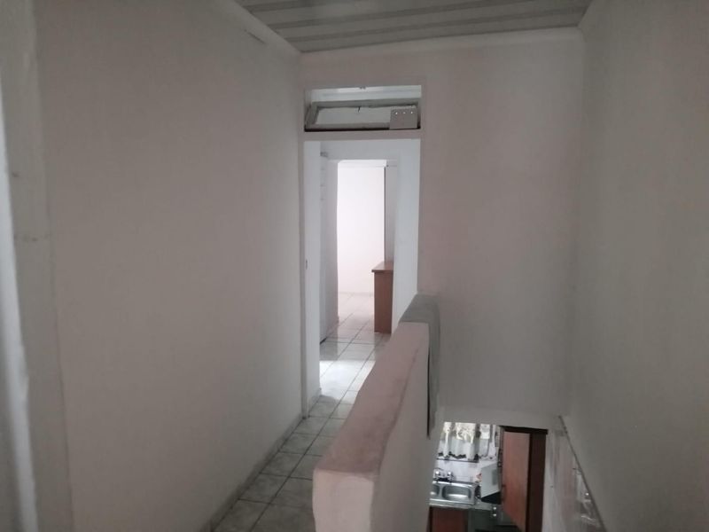 A view of an interior hallway with tiled flooring, leading to adjacent rooms, featuring a staircase balustrade and neutral wall finishes.