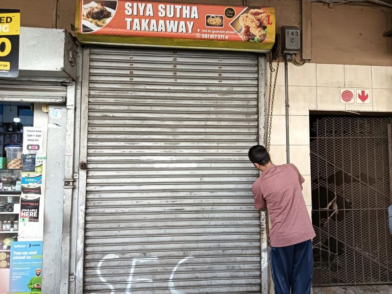 Street-level commercial storefront featuring a metal roller shutter door, signage, and a security gate entrance.