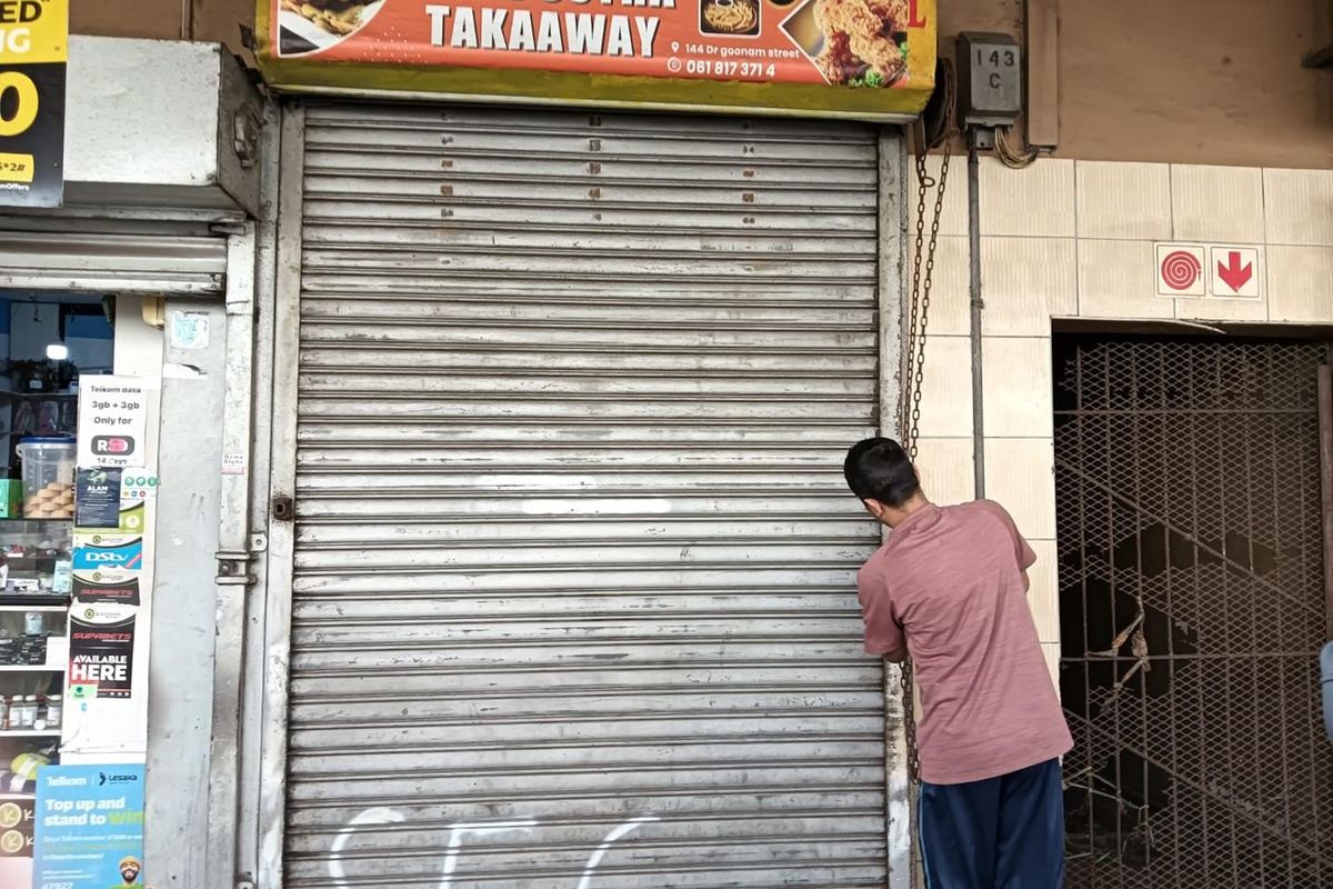 Street-level commercial storefront featuring a metal roller shutter door, signage, and a security gate entrance.