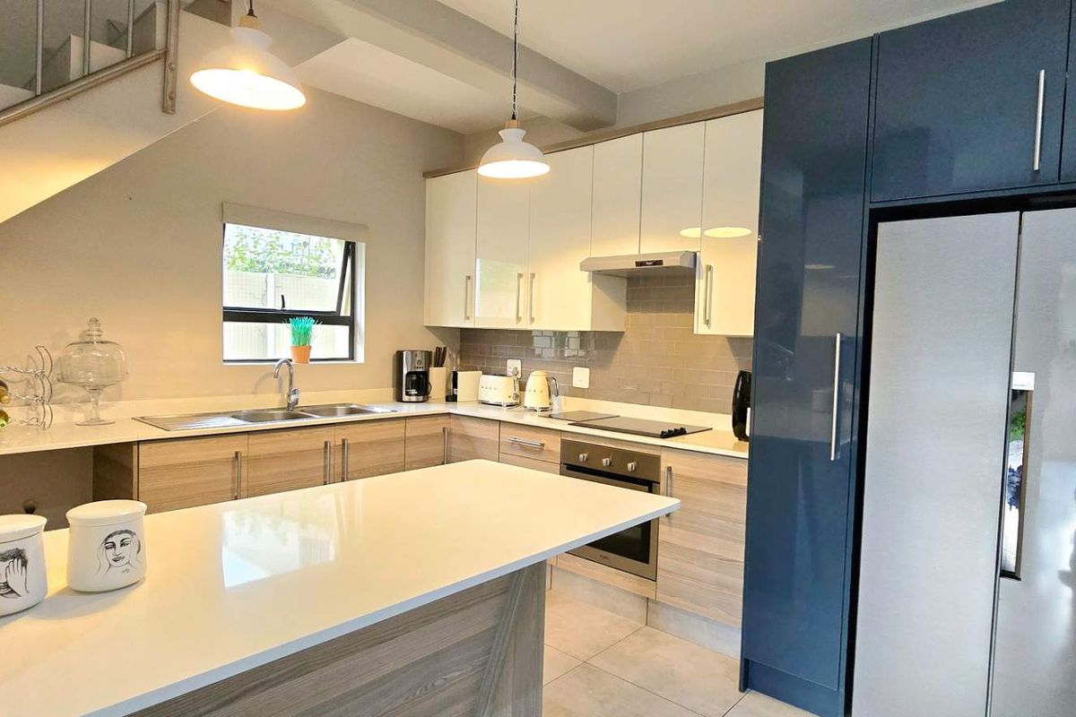 Modern kitchen featuring two-tone cabinetry, quartz countertops, a central island, and integrated appliances, situated beneath a staircase.