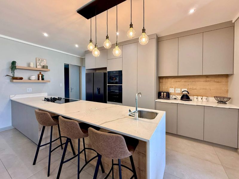 Modern kitchen featuring sleek handleless cabinetry, quartz countertops, a central island with integrated gas hob and sink, and stylish pendant lighting.