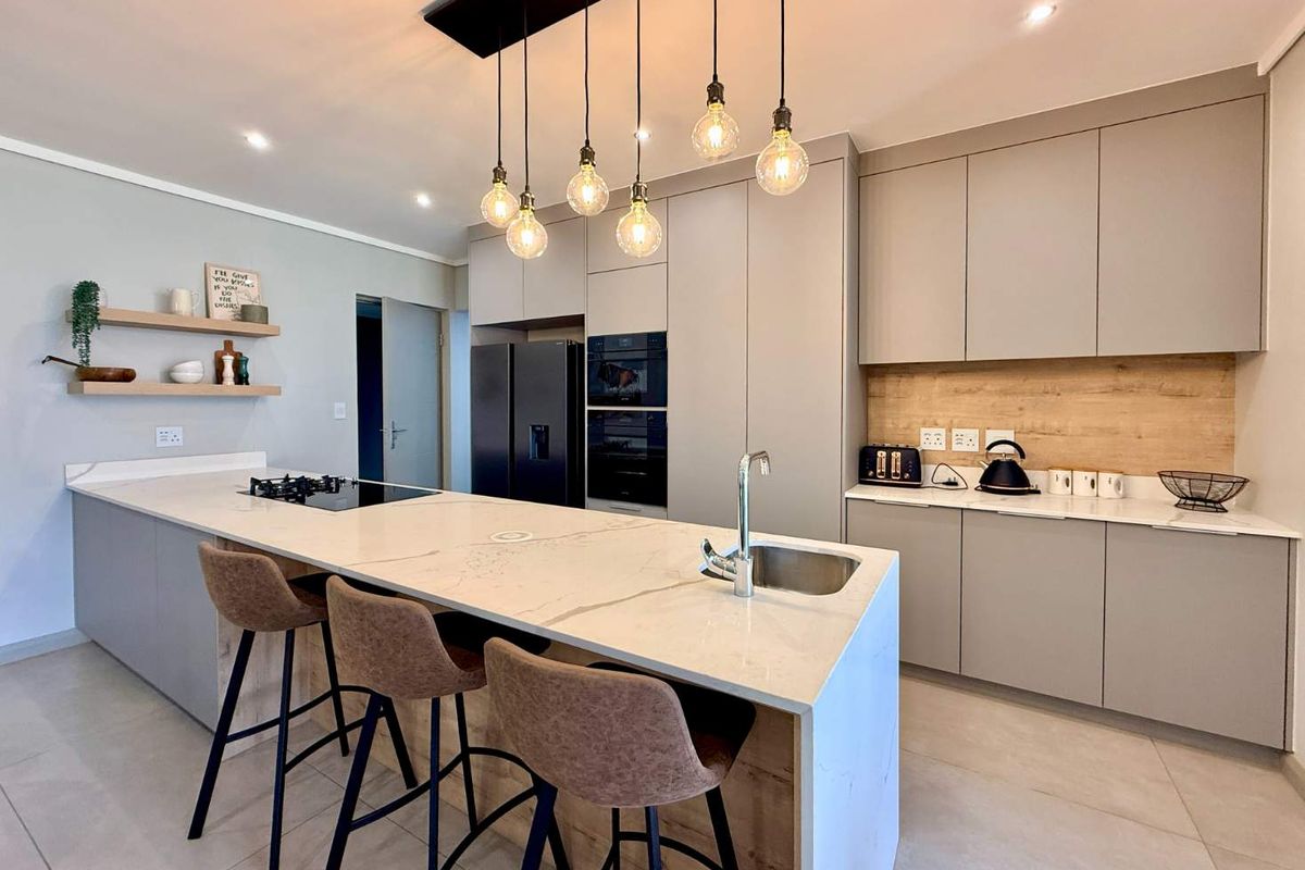 Modern kitchen featuring sleek handleless cabinetry, quartz countertops, a central island with integrated gas hob and sink, and stylish pendant lighting.