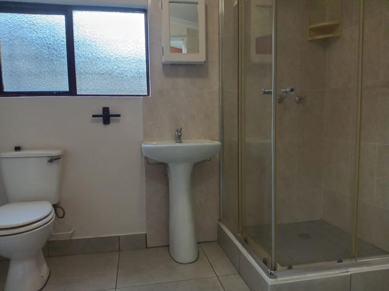 A functional bathroom featuring a pedestal washbasin, toilet, and a glass-enclosed shower with tiled finishes and an obscured glass window.