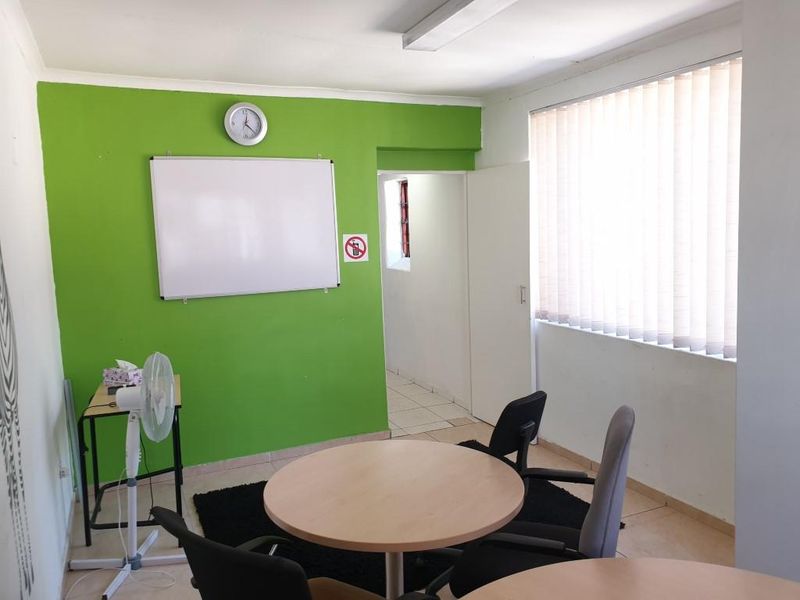A functional office space featuring tiled flooring, vertical window blinds, and bright green accent wall paint, suitable for a professional work environment.