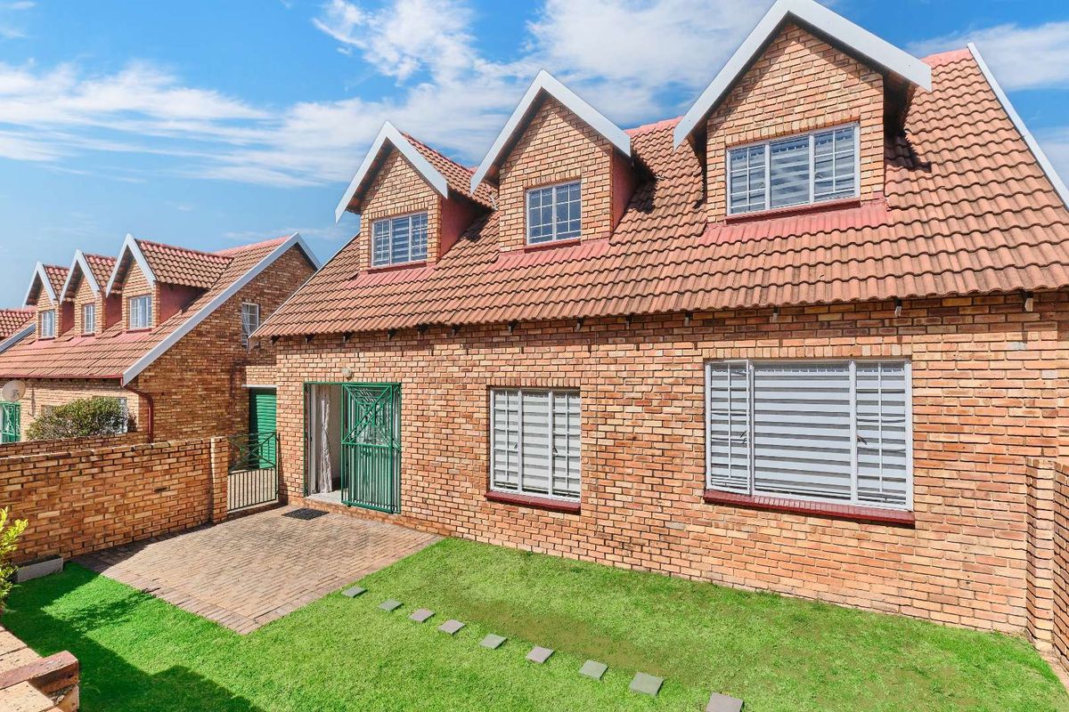 Rear view of a face brick townhouse featuring a paved patio, small garden, and dormer windows under a tiled roof.