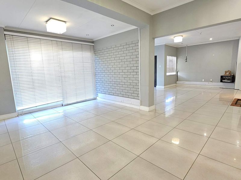Spacious open-plan living area featuring large format floor tiles, a brick feature wall, fireplace, and sliding doors leading to the exterior.