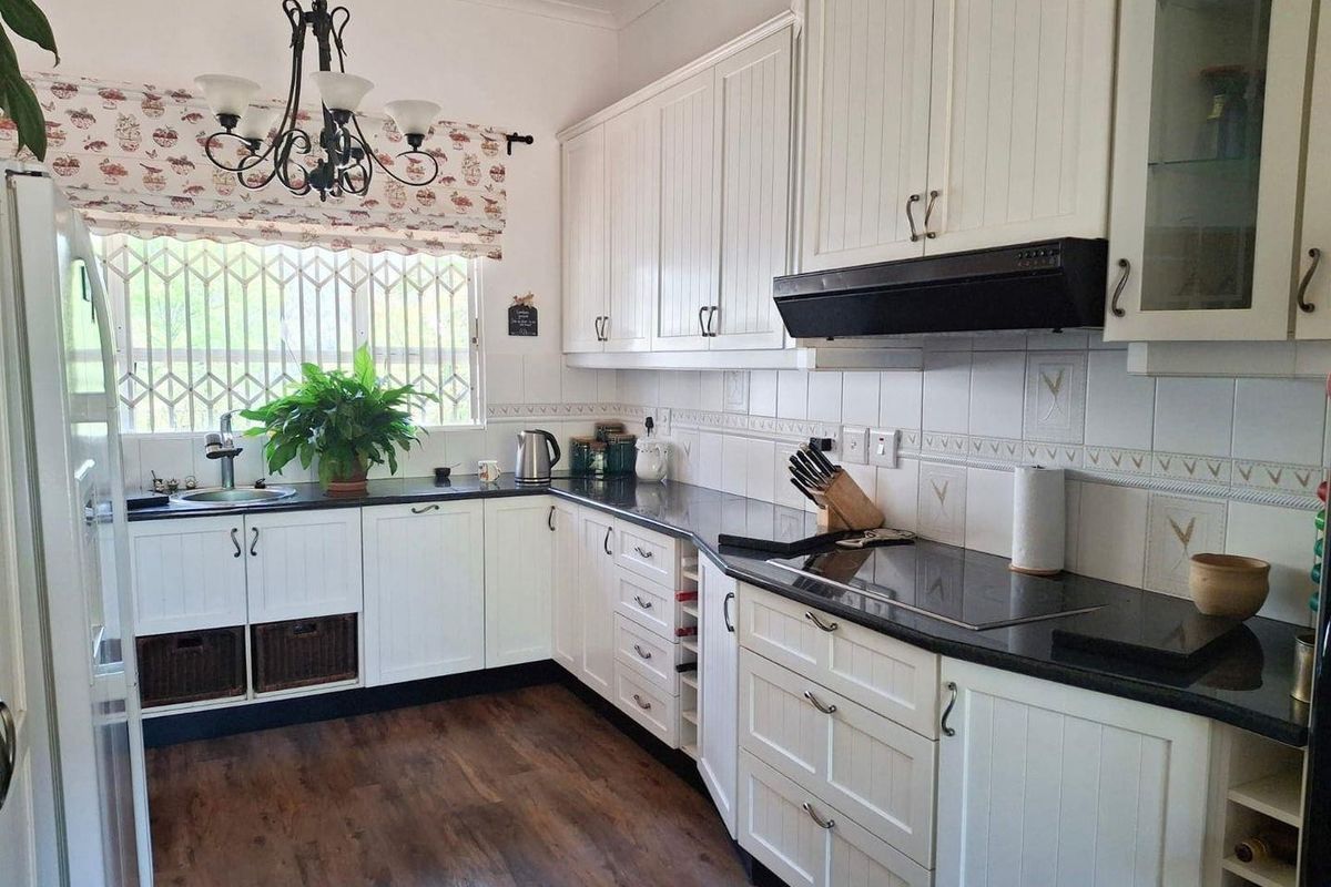A functional kitchen featuring white cabinetry, dark countertops, a built-in hob, and an extractor fan, with a window overlooking the exterior.