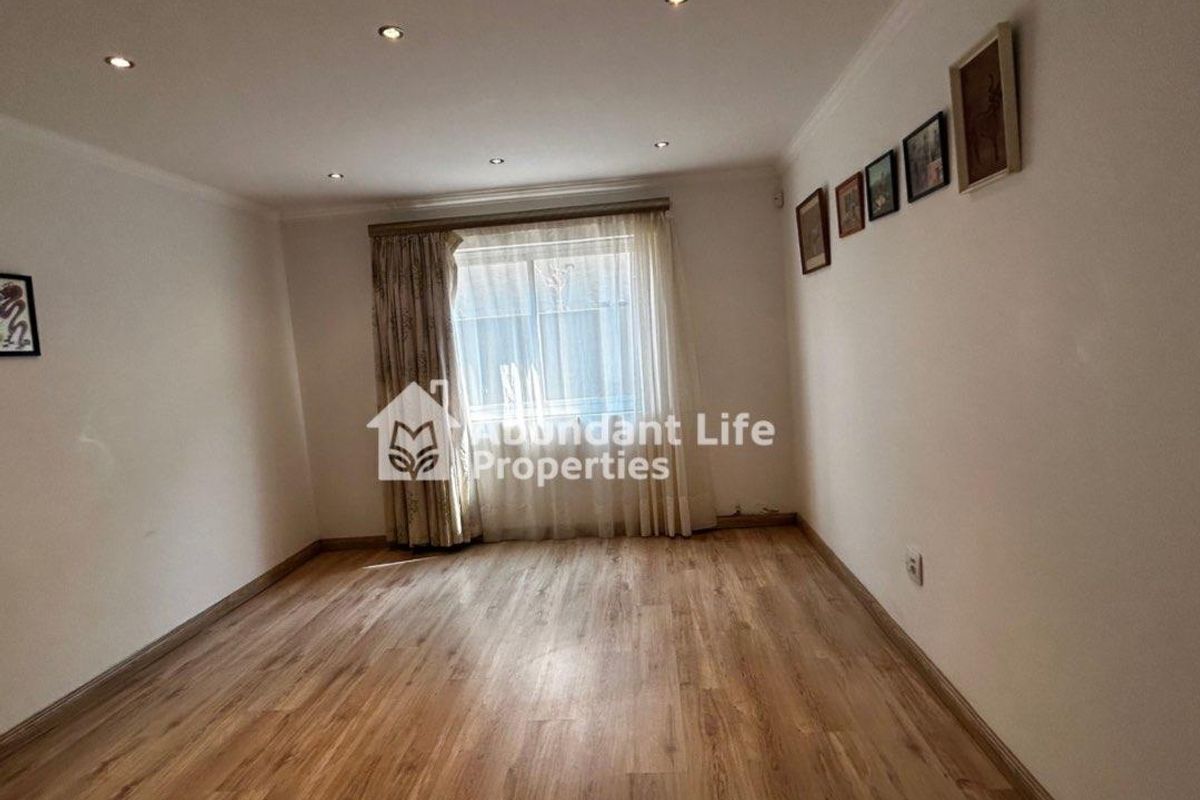 A bright, empty living room featuring modern laminate flooring, recessed downlights, and neutral walls, offering a versatile space ready for personalization.