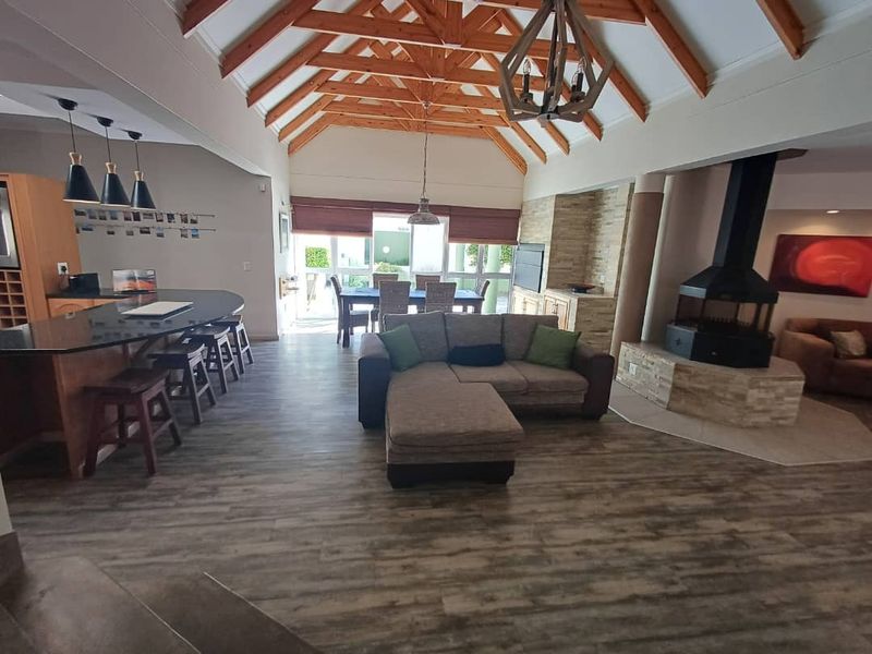 Spacious open-plan living area featuring a vaulted timber-beamed ceiling, a central freestanding fireplace with stone cladding, and a modern kitchen with a breakfast bar.