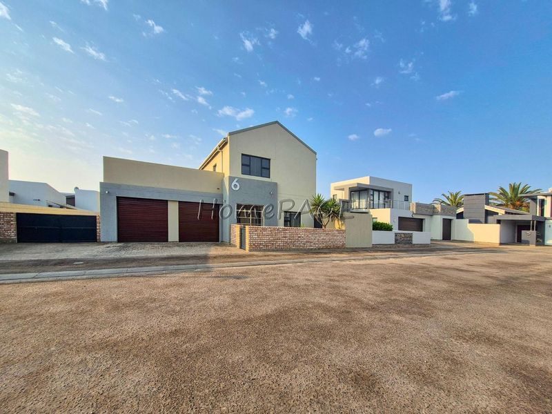 Front elevation of a modern double-storey house featuring a double garage, paved driveway, and brick boundary wall.