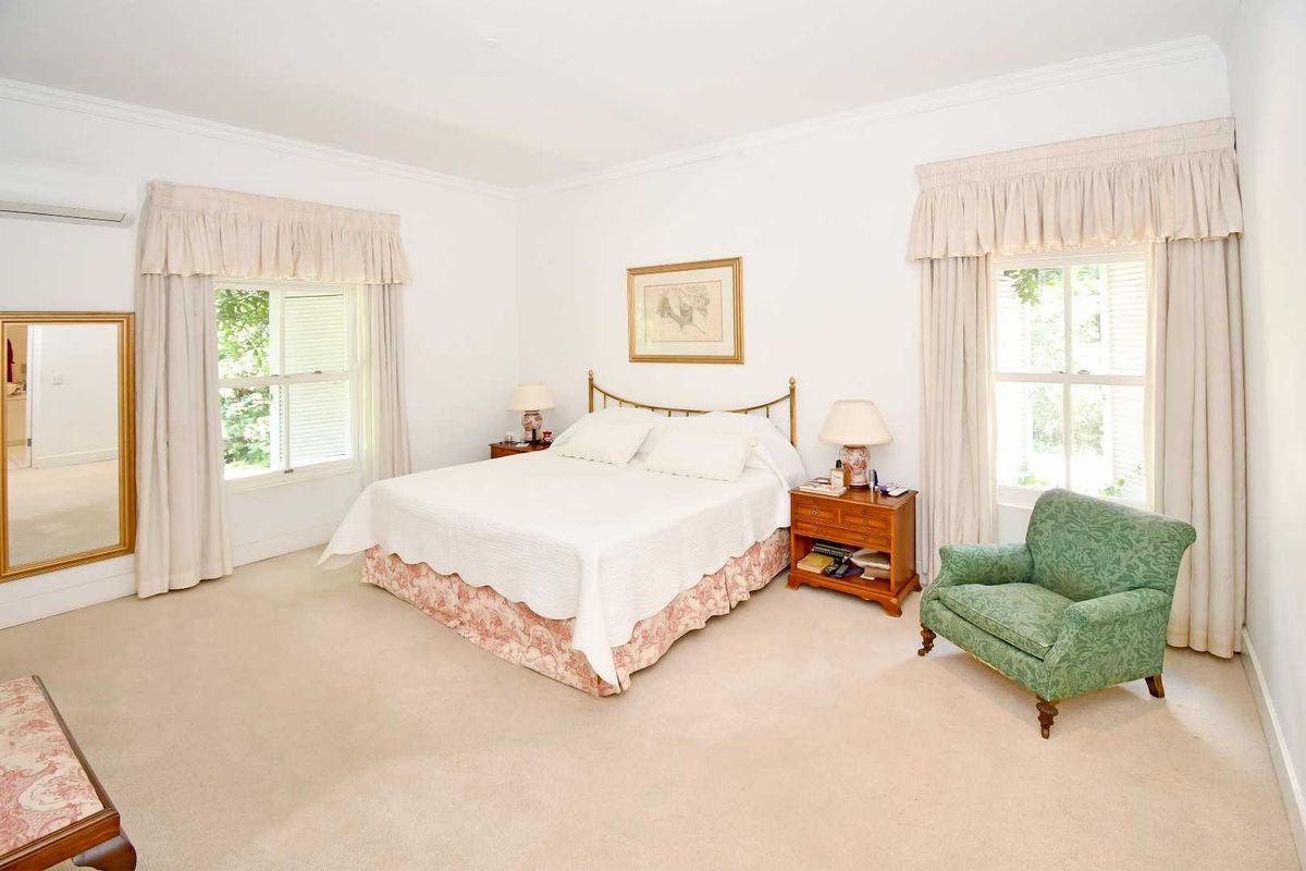 Spacious bedroom featuring neutral carpeting, dual windows with classic drapery, and a wall-mounted air conditioning unit.