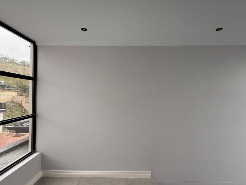 A bright, modern, and empty bedroom featuring large black-framed windows, recessed downlights, and neutral tiled flooring, offering a clean canvas for interior design.