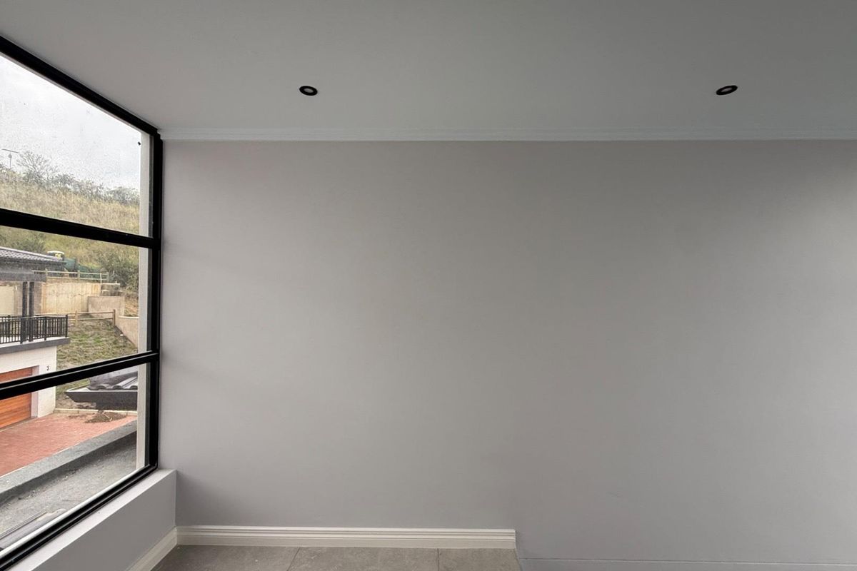 A bright, modern, and empty bedroom featuring large black-framed windows, recessed downlights, and neutral tiled flooring, offering a clean canvas for interior design.