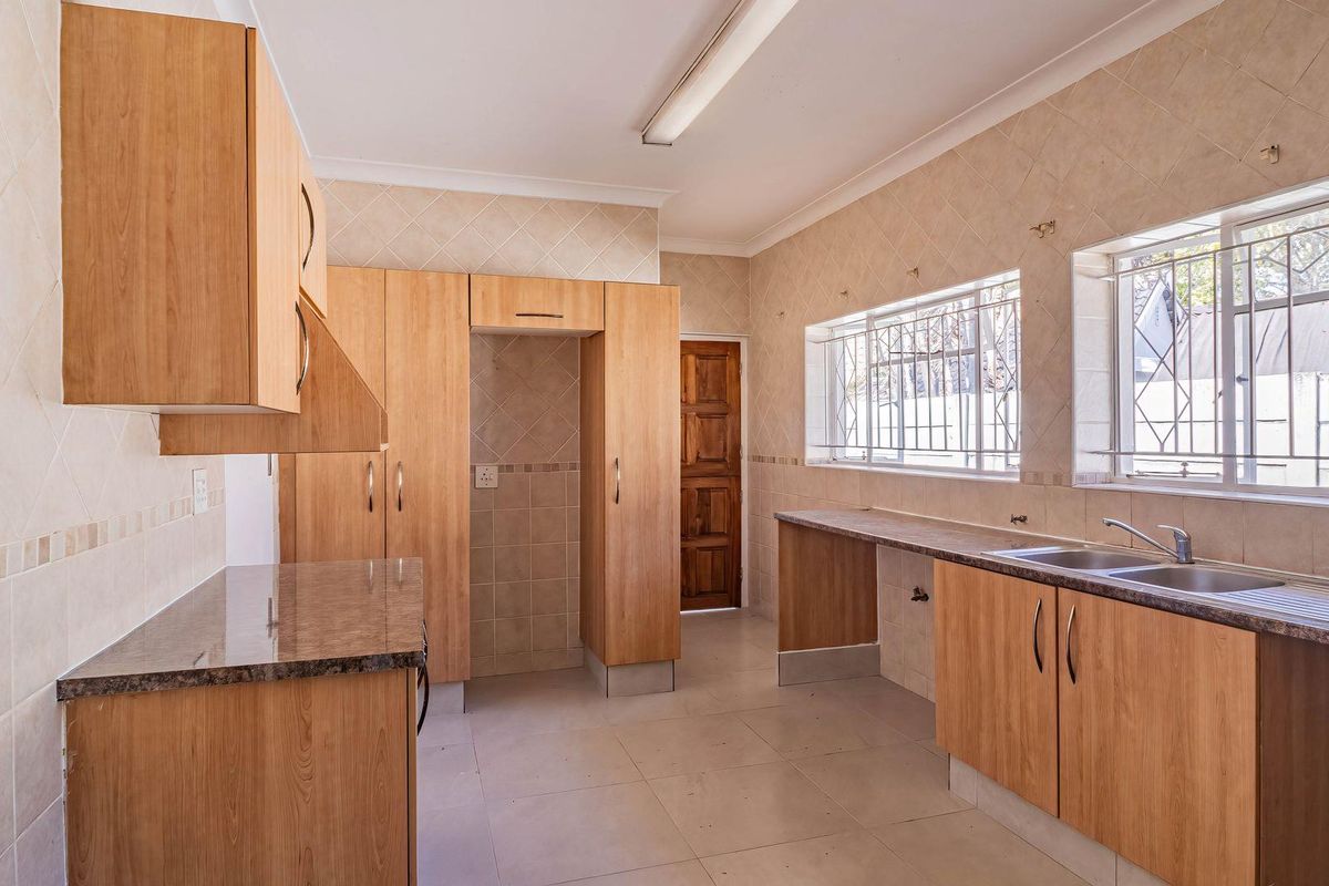 A functional kitchen featuring light wood cabinetry, granite-look countertops, tiled walls, and double stainless steel sink with security bars on windows.