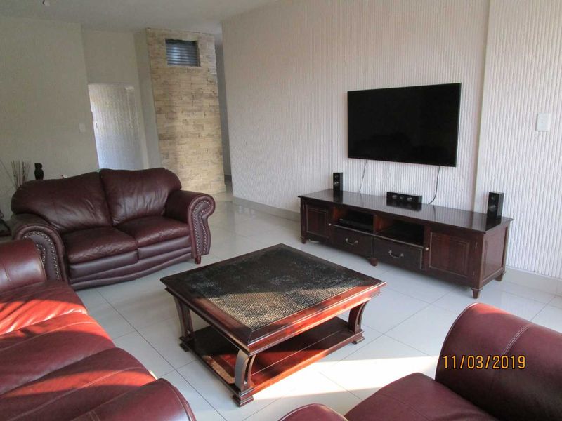 A living room featuring tiled flooring, a textured accent wall, and a stone-clad pillar detail.