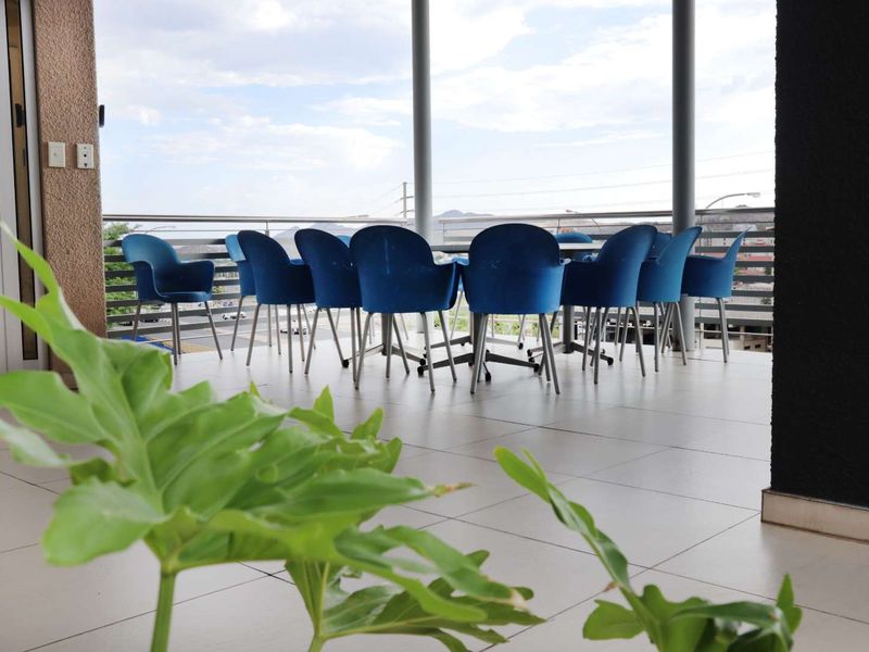 A spacious covered balcony featuring tiled flooring, metal railings, and support columns, offering an open-air setting suitable for office breakout or meeting space.