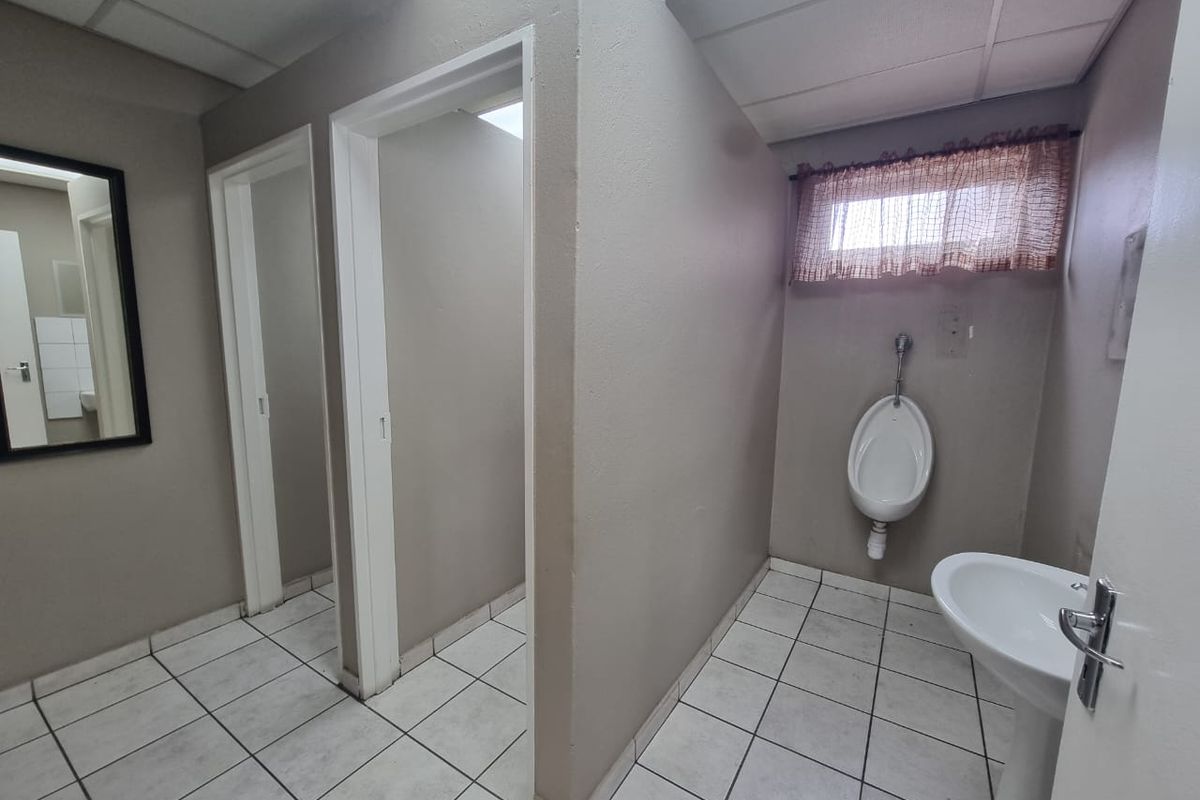 A functional commercial-style bathroom featuring a wall-mounted urinal, pedestal basin, tiled flooring, and partitioned cubicle access.