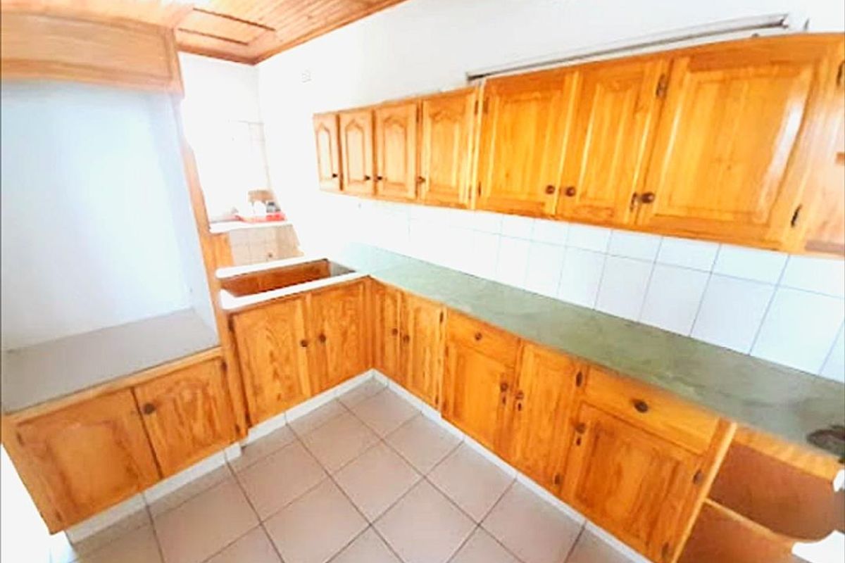A functional kitchen featuring extensive wooden cabinetry, tiled flooring, and a tiled backsplash, offering a traditional aesthetic with ample storage space.