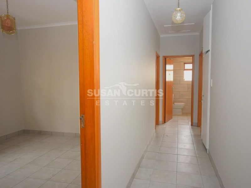 A clean, neutral hallway featuring tiled flooring and wooden door frames, providing access to adjacent rooms and a bathroom.