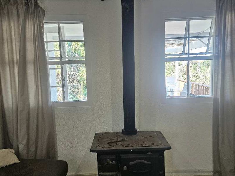 Living area featuring a traditional cast iron wood-burning stove, tiled flooring, and dual casement windows providing natural light.