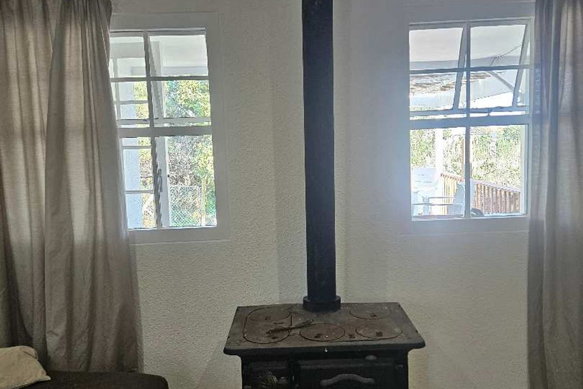 Living area featuring a traditional cast iron wood-burning stove, tiled flooring, and dual casement windows providing natural light.