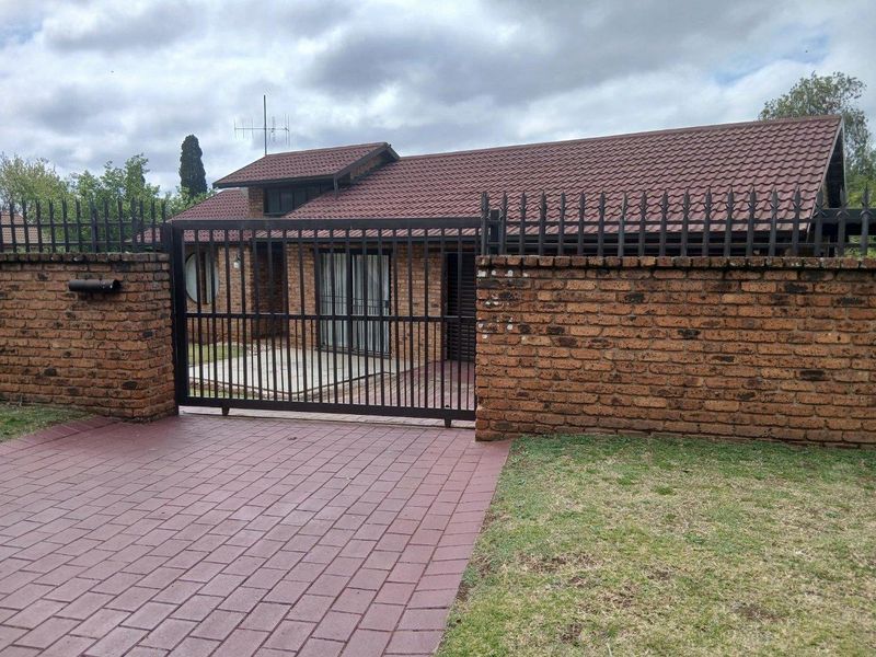 Front view of a facebrick house featuring a paved driveway, secure metal gate, and a tiled roof with a private front courtyard area.