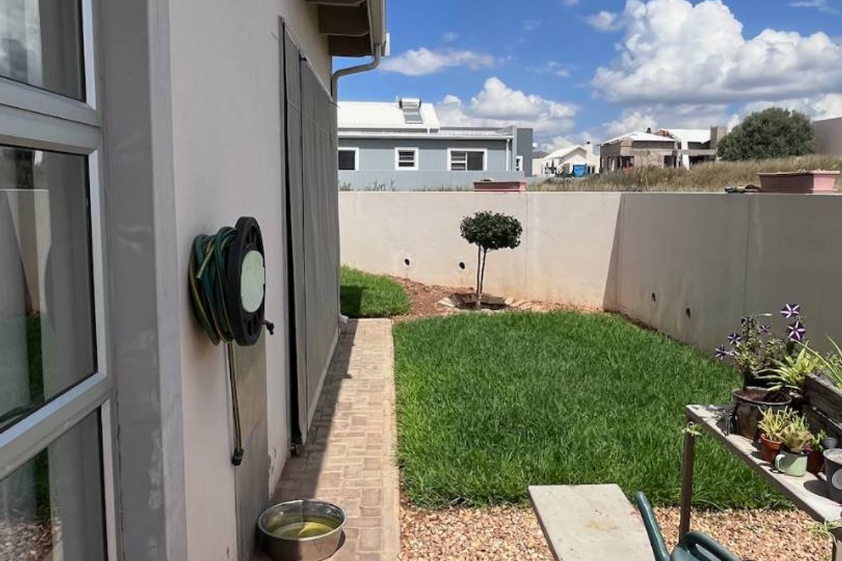 A side garden area featuring a paved walkway, a well-maintained lawn, and a secure boundary wall.