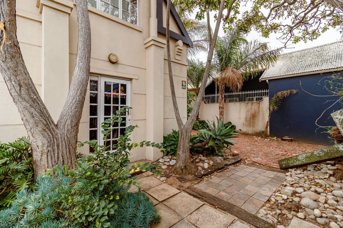 A view of the rear exterior area featuring a paved patio, established garden landscaping, and access to the main dwelling through a glass-paned door.