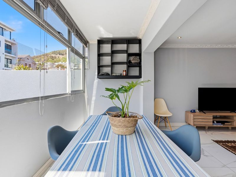 Bright open-plan living and dining area featuring large windows, tiled flooring, recessed lighting, and decorative ceiling cornices, offering a clean and functional space.