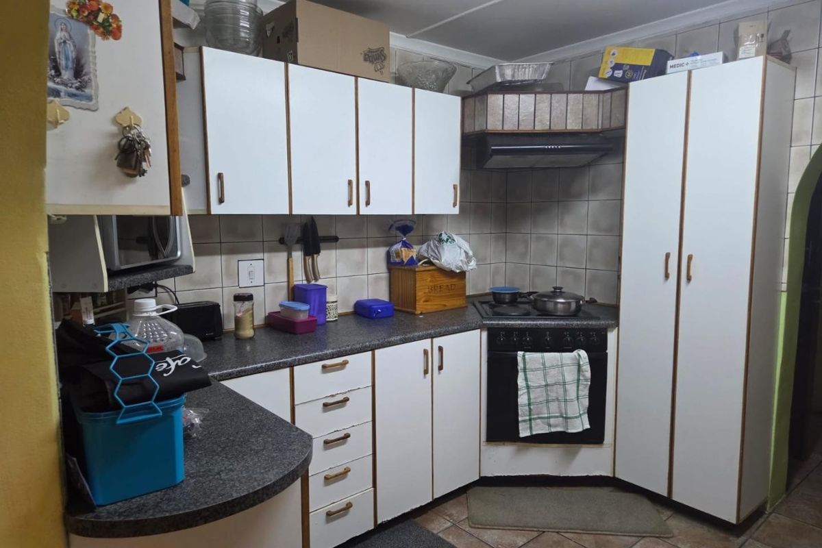 A functional kitchen featuring white laminate cabinetry, dark countertops, a built-in oven with hob, and tiled backsplash and flooring.
