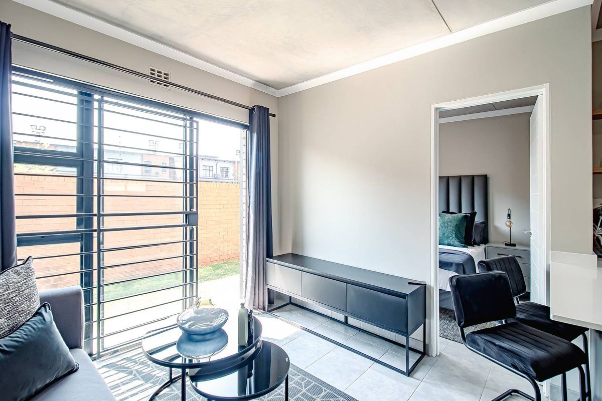 A bright living area featuring tiled flooring, a sliding glass door with security gate, and direct access to an outdoor space.