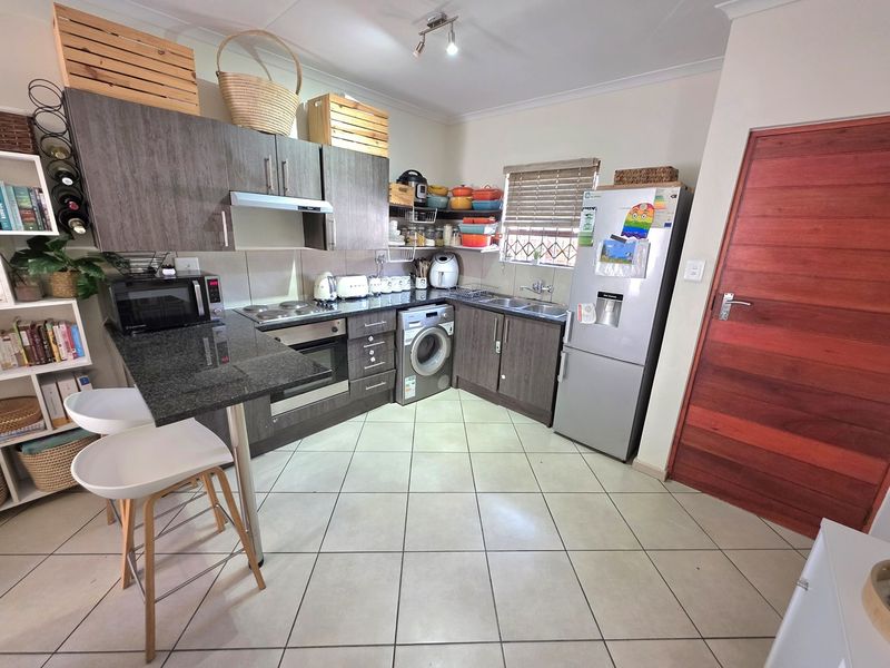 Compact kitchen featuring granite countertops, built-in oven, electric hob, extractor fan, and integrated laundry plumbing, finished with tiled flooring and modern cabinetry.