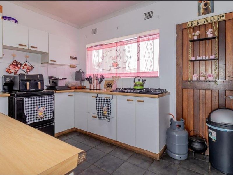A functional kitchen featuring white cabinetry, a gas hob, freestanding oven, and tiled flooring, with a rustic timber door and security-barred window.